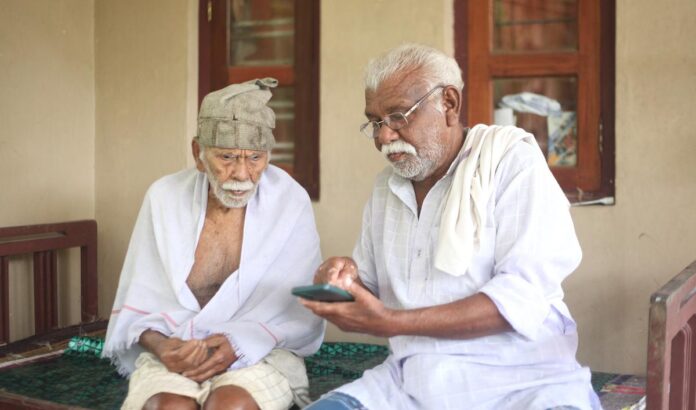 103 वर्षीय करुणक पानिकर और उनके बेटे, राजन, तिरुवनंतपुरम के पुलमपरा पंचायत में अपने घर पर YouTube पर एक गीत देख रहे हैं।