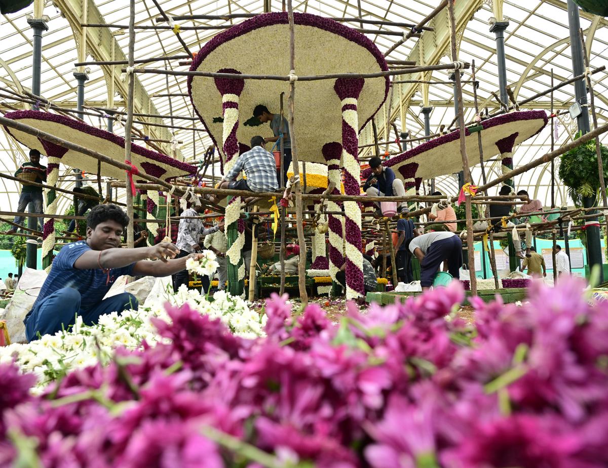 श्रमिक 5 अगस्त, 2025 को बेंगलुरु में 218 वें फ्लावर शो से आगे लालबाग ग्लास हाउस में विभिन्न प्रकार के फूलों का उपयोग करके मॉडल बनाते हैं।  