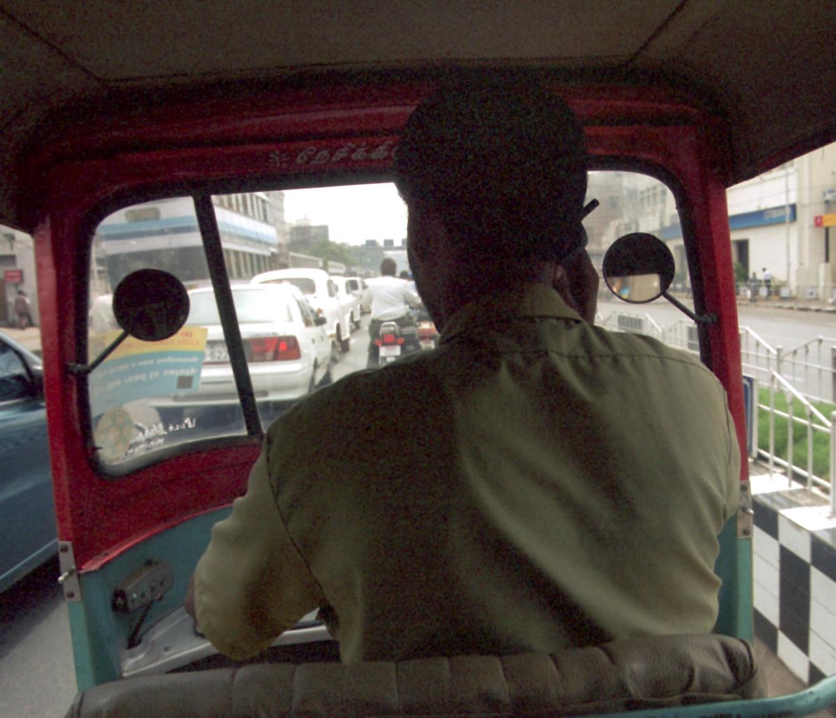 एक ऑटोरिक्शा ड्राइवर मोबाइल फोन का उपयोग करते हुए चलते समय।