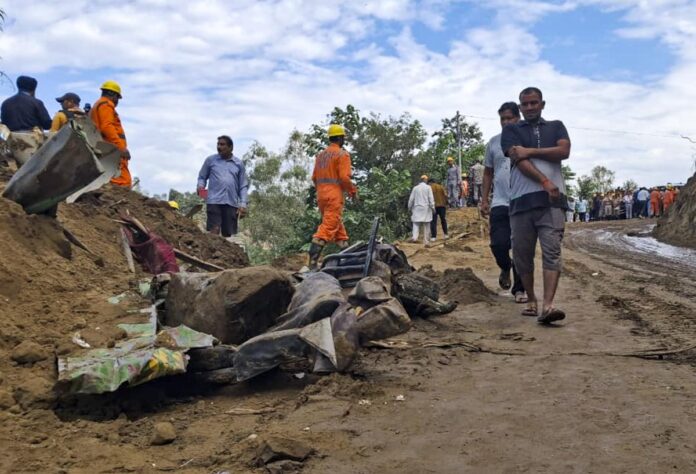 बिलासपुर में मलबे में पड़ी बस के क्षतिग्रस्त अवशेषों के पास से गुजरते लोग